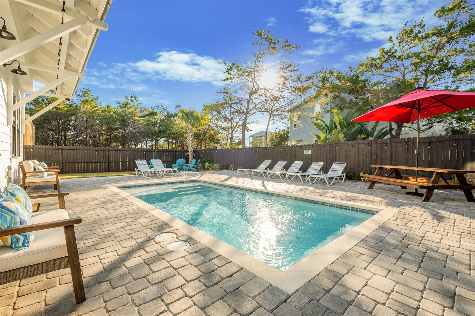 Unwind by the pool in this serene backyard, complete with comfortable seating, a red umbrella for shade, and plenty of space for family fun.