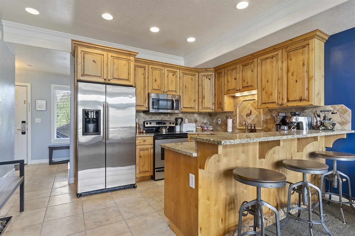 A chef-inspired kitchen showcasing rich wood cabinetry, gleaming countertops, and bar seating—ideal for casual dining or hosting with ease.