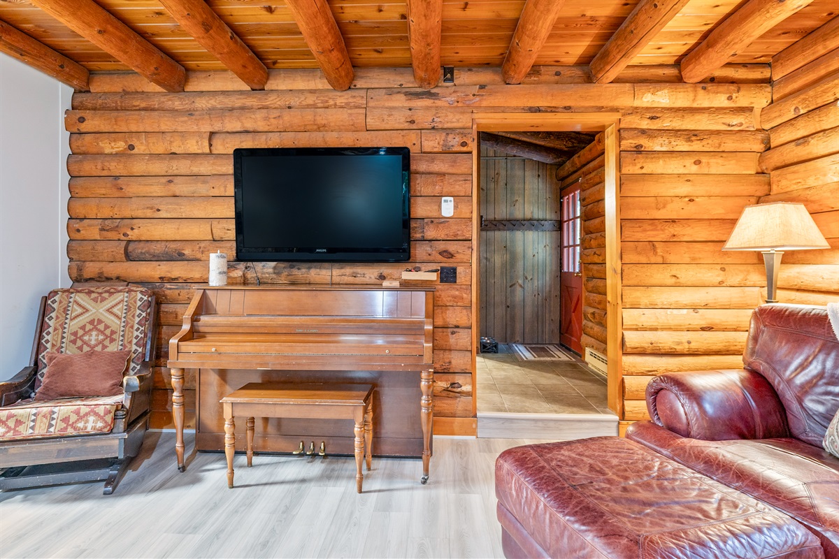 Gather in this warm log cabin living space featuring a mounted flat-screen TV, upright piano, and rustic seating for family entertainment.