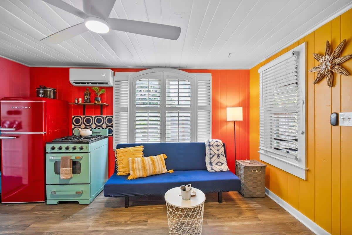 The open plan means whoever is cooking is never shut away on their own. Ceiling fan turning, mini-split humming quietly, blue sofa a few steps away for whoever is supervising rather than actually helping.
