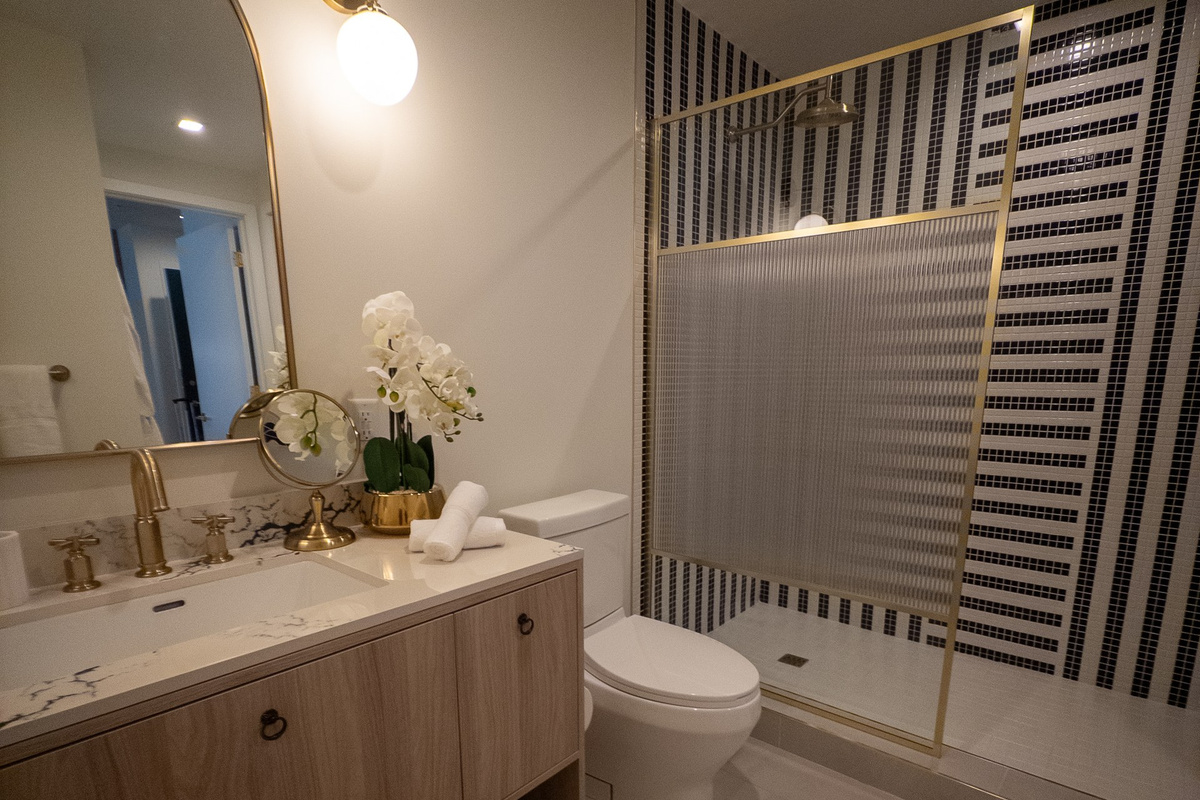 Start the day in a spa-style bath with a walk-in rainfall shower, designer tilework and warm brushed-gold fixtures.