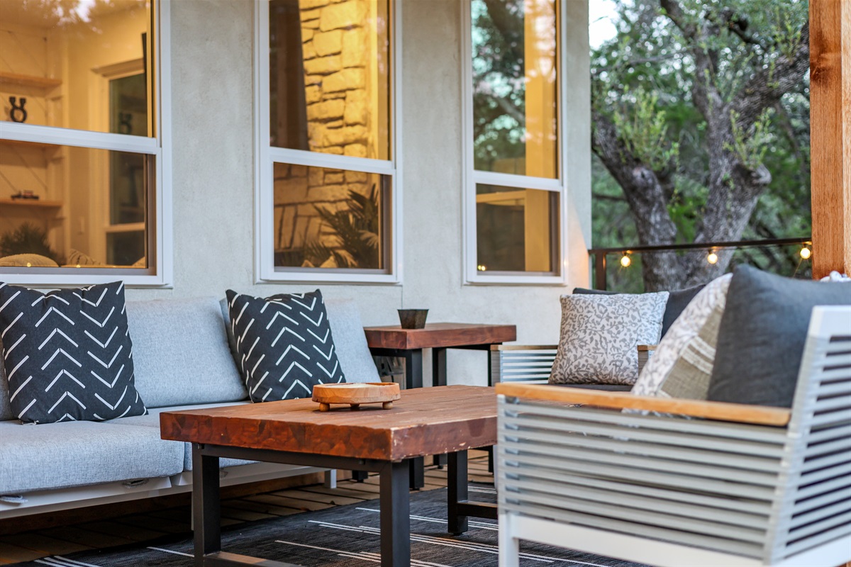This modern porch space blends comfort and charm with stylish cushions, a natural wood coffee table, and views of the surrounding trees — ideal for morning coffee or late-night chats.