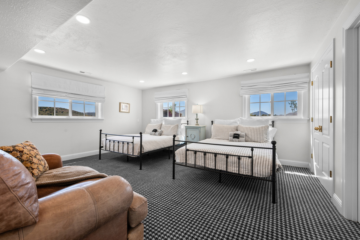 This generous bedroom features two queen-size beds, a cozy sofa, abundant natural light, mountain views, and plenty of room for guests to relax comfortably.