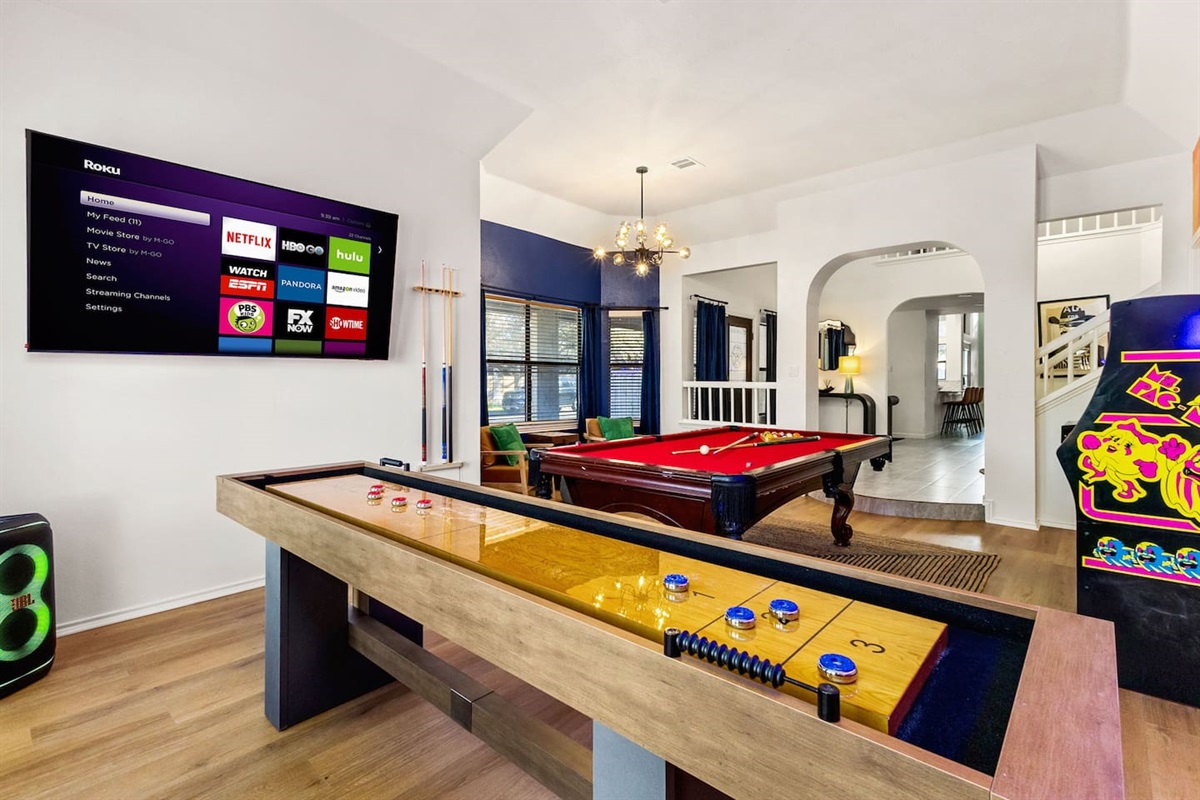 This fun-filled game zone features a shuffleboard table, pool table, smart TV with streaming apps, vintage arcade game, and sleek decor—perfect for hosting game nights or just kicking back in style with friends and family.