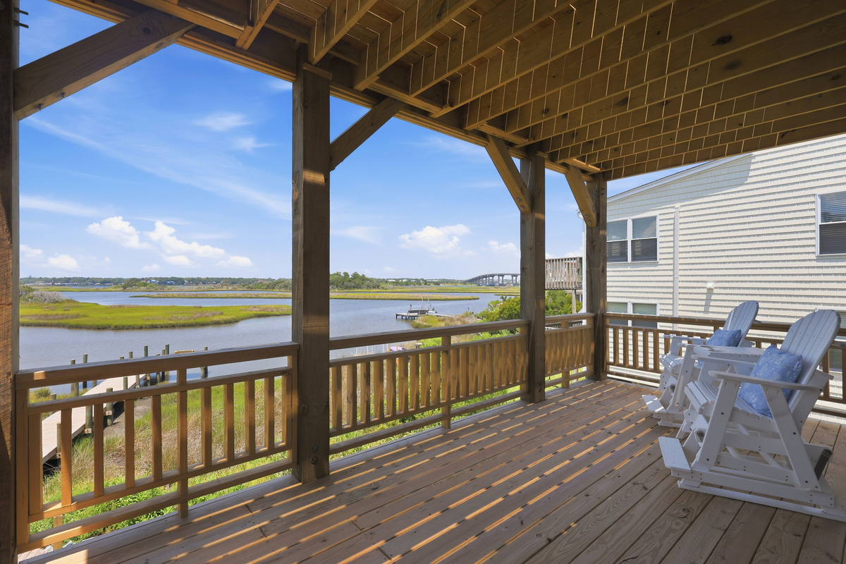 The covered lower deck offers a shaded retreat with rocking Adirondack chairs, perfect for enjoying the coastal breeze and scenic waterfront views