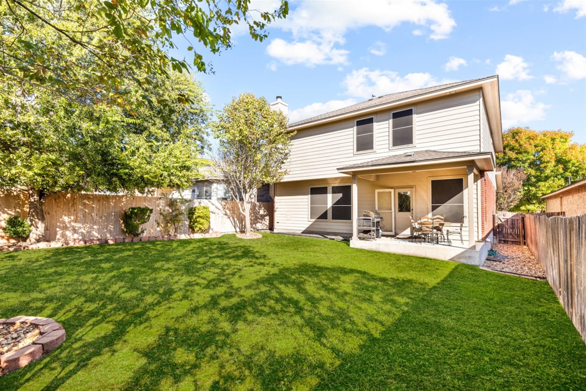 Spacious fenced backyard with BBQ gas grill, outdoor dining, and furniture for family cookouts or gatherings.