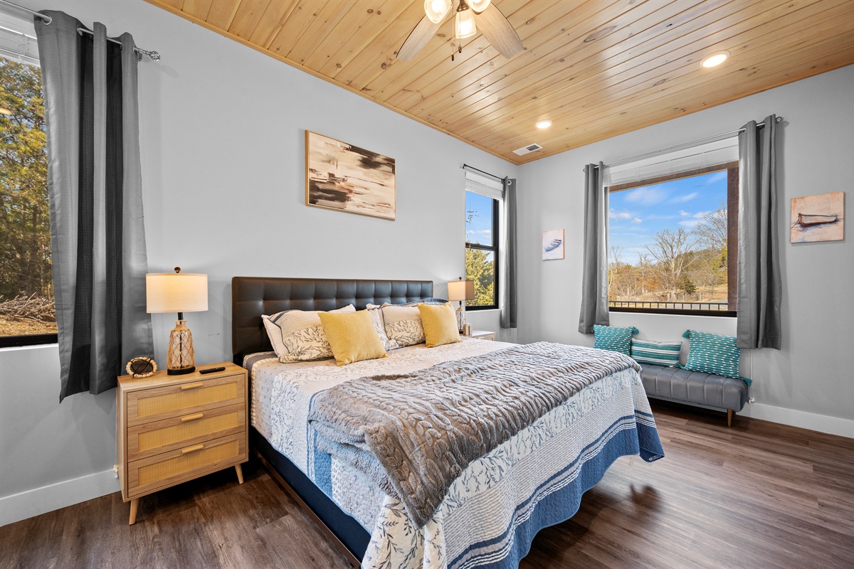 Bedroom with plush bedding, wood ceilings, and large windows that bring in natural light and views of the surrounding area.