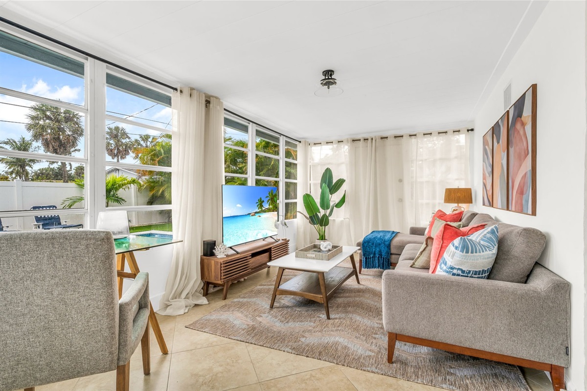 A beautifully designed Florida sunroom with wrap-around windows, modern furnishings, a Smart Fire streaming TV, and tranquil pool views—ideal for lounging, morning coffee, or working in style.