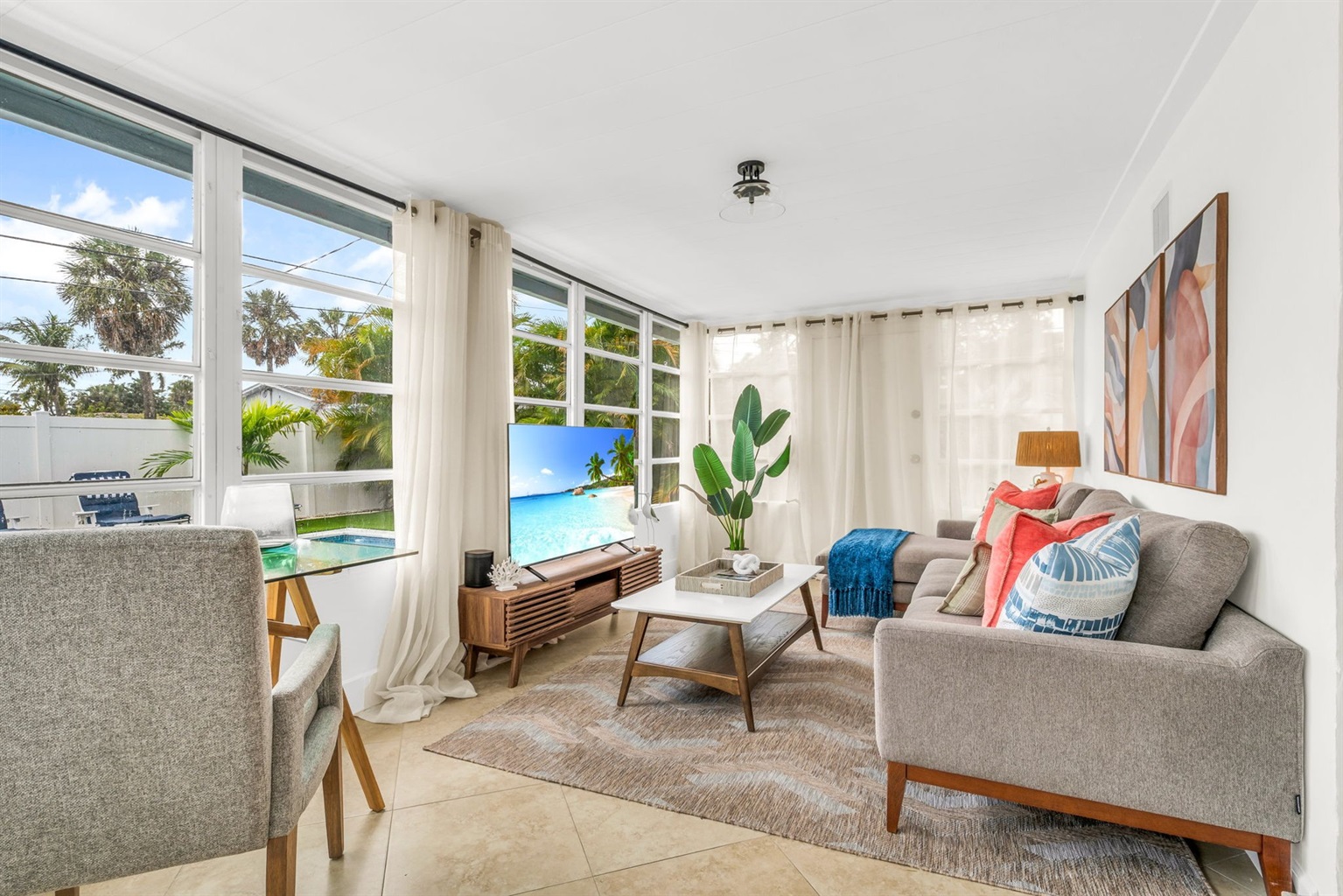 A beautifully designed Florida sunroom with wrap-around windows, modern furnishings, a Smart Fire streaming TV, and tranquil pool views—ideal for lounging, morning coffee, or working in style.