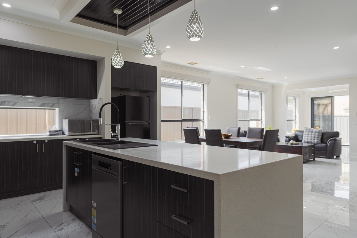 Open-plan kitchen, dining and living area with island bench, dishwasher, microwave and fridge.