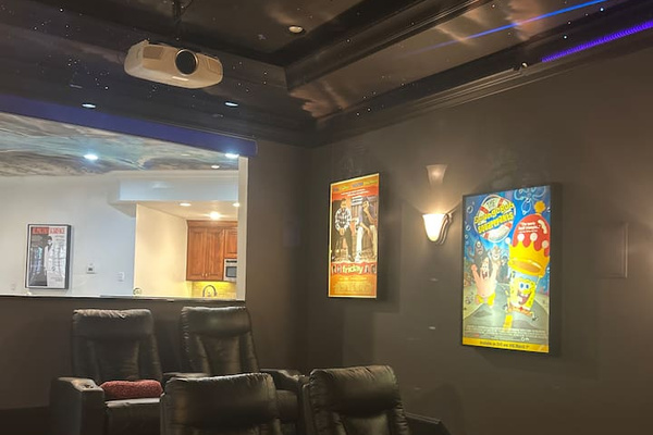 Dedicated home theater with tiered leather recliner seating, ceiling-mounted projector, surround sound, star-themed ceiling, movie posters, wall sconces, and dark finishes for a true cinematic experience.