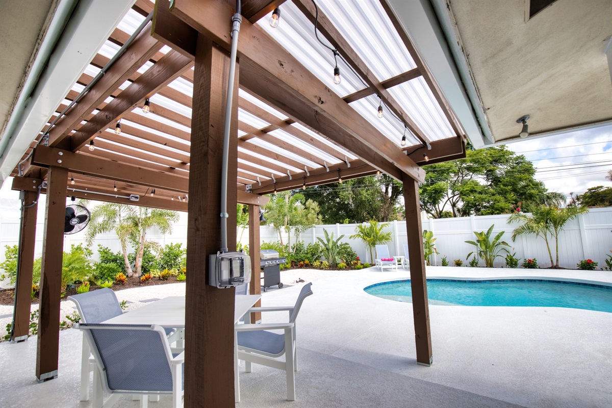 Patio area with covered pergola, dining table with four chairs, 65" TV and fan to keep you cool.