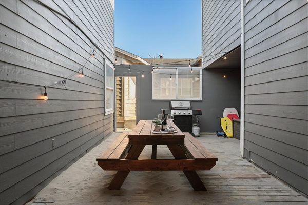 Private enclosed outdoor courtyard with table, bbq, box of toys, and hanging lights for ambiance. 