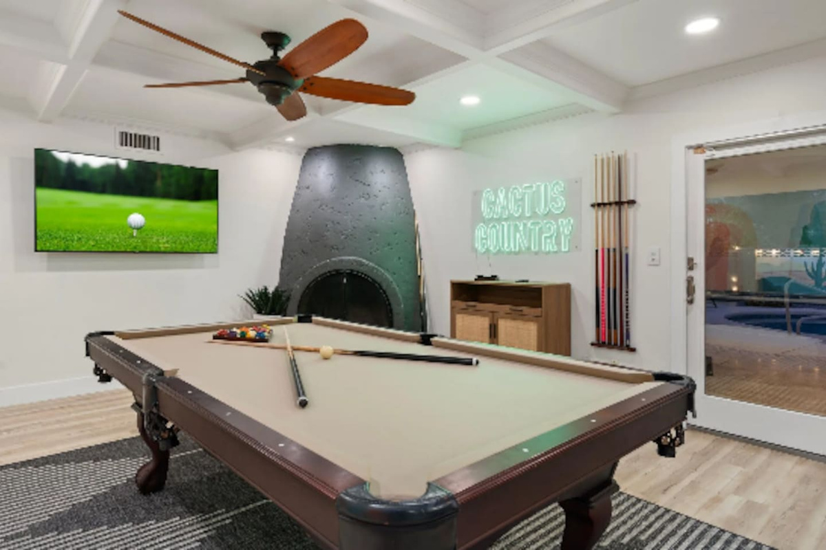 A stone fireplace adds warmth to game nights, with the pool table and neon signage making this room feel like a private lounge.