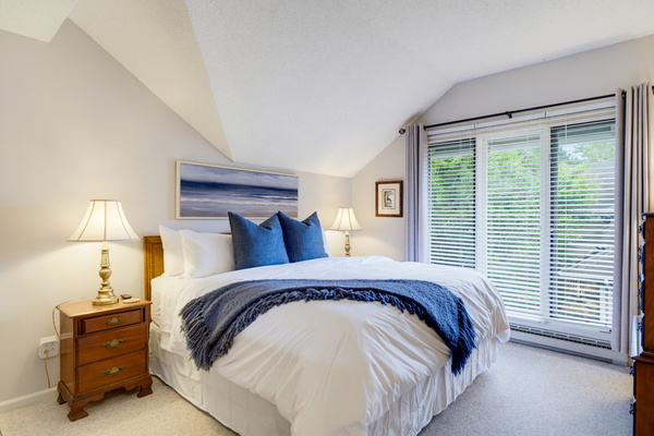 You rest easy in the primary bedroom with king bed, luxury bedding, architectural ceiling, and a wall of windows bringing in the mountain light.