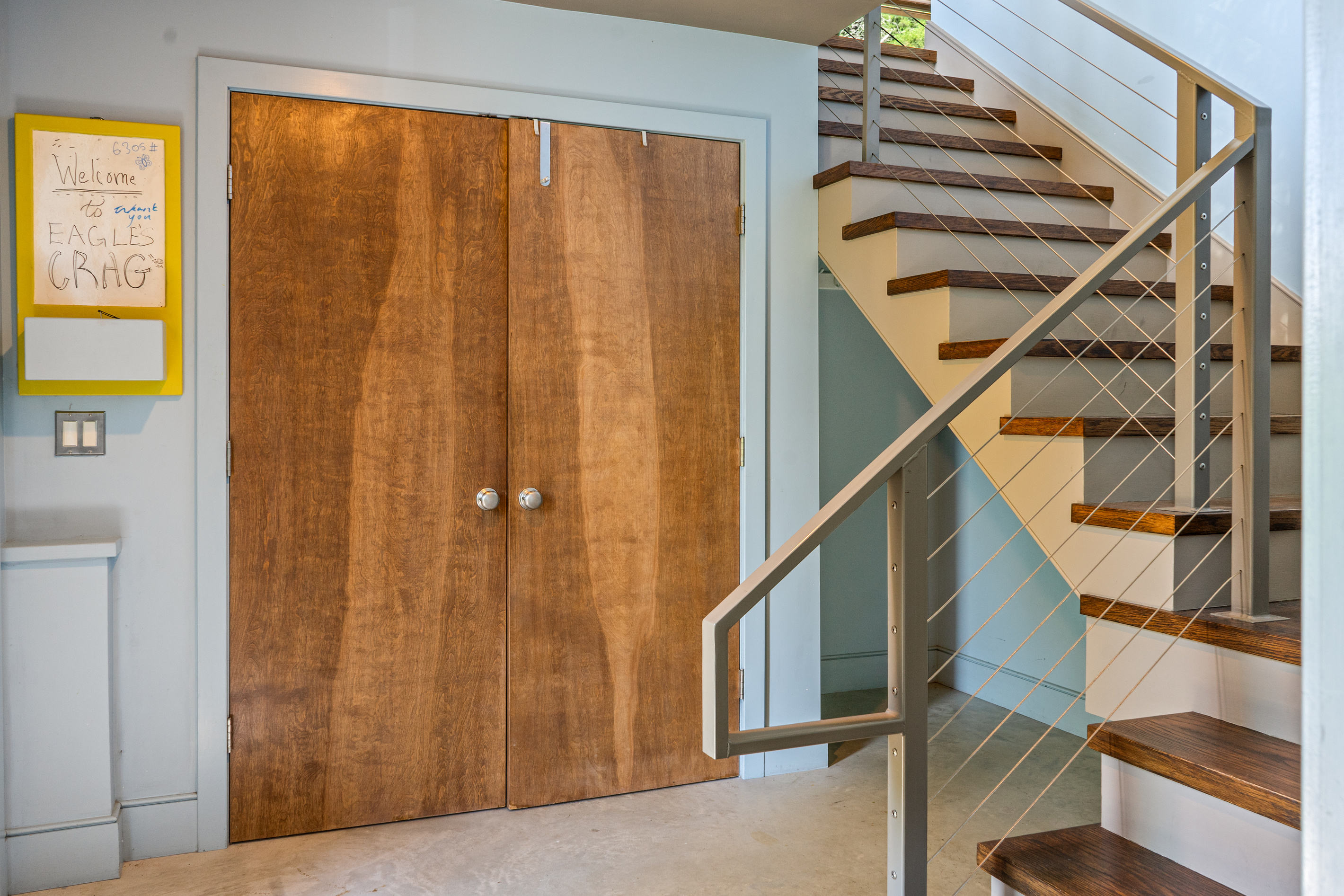 "The Crag's" Base Camp entryway features double coat closets, concrete floors, and custom cable-rail stairs. Designed for seamless gear drop-offs before ascending to the main Social Heart. Your gateway to Acadia National Park.