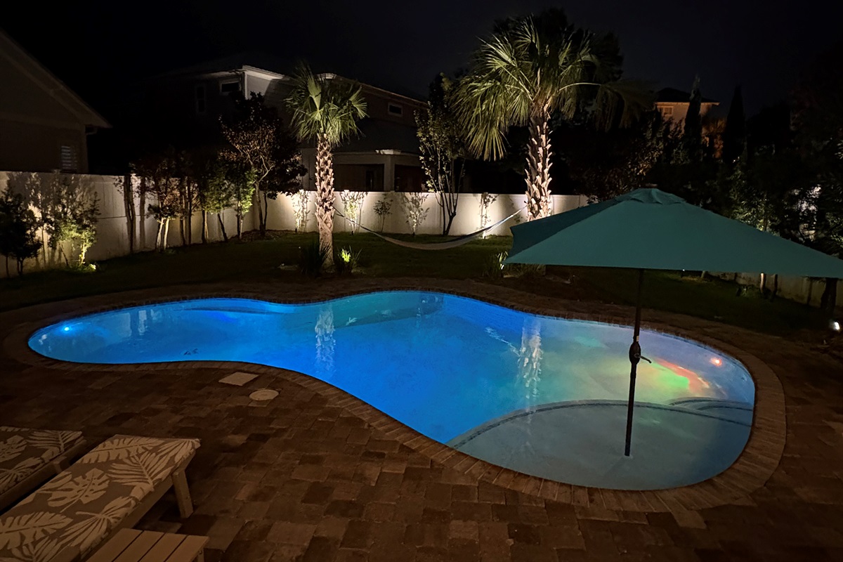 Nighttime view of the illuminated private pool and landscaped backyard.