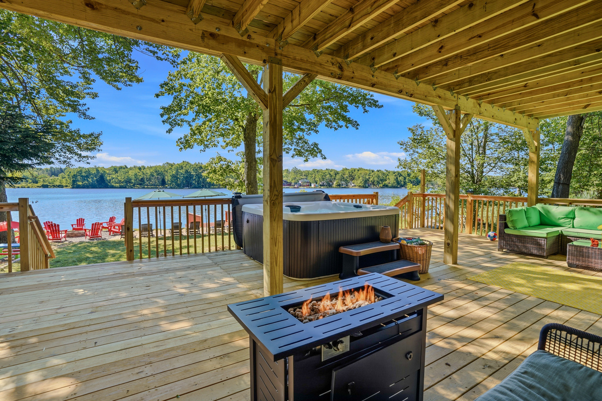 Lower deck with fire table, hot tub, and unobstructed lake views through the tree canopy