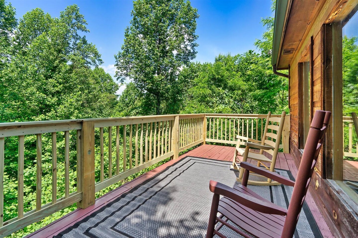 A serene cabin deck with rustic rocking chairs invites you to unwind while taking in the stunning natural surroundings and enjoying the sounds of nature.