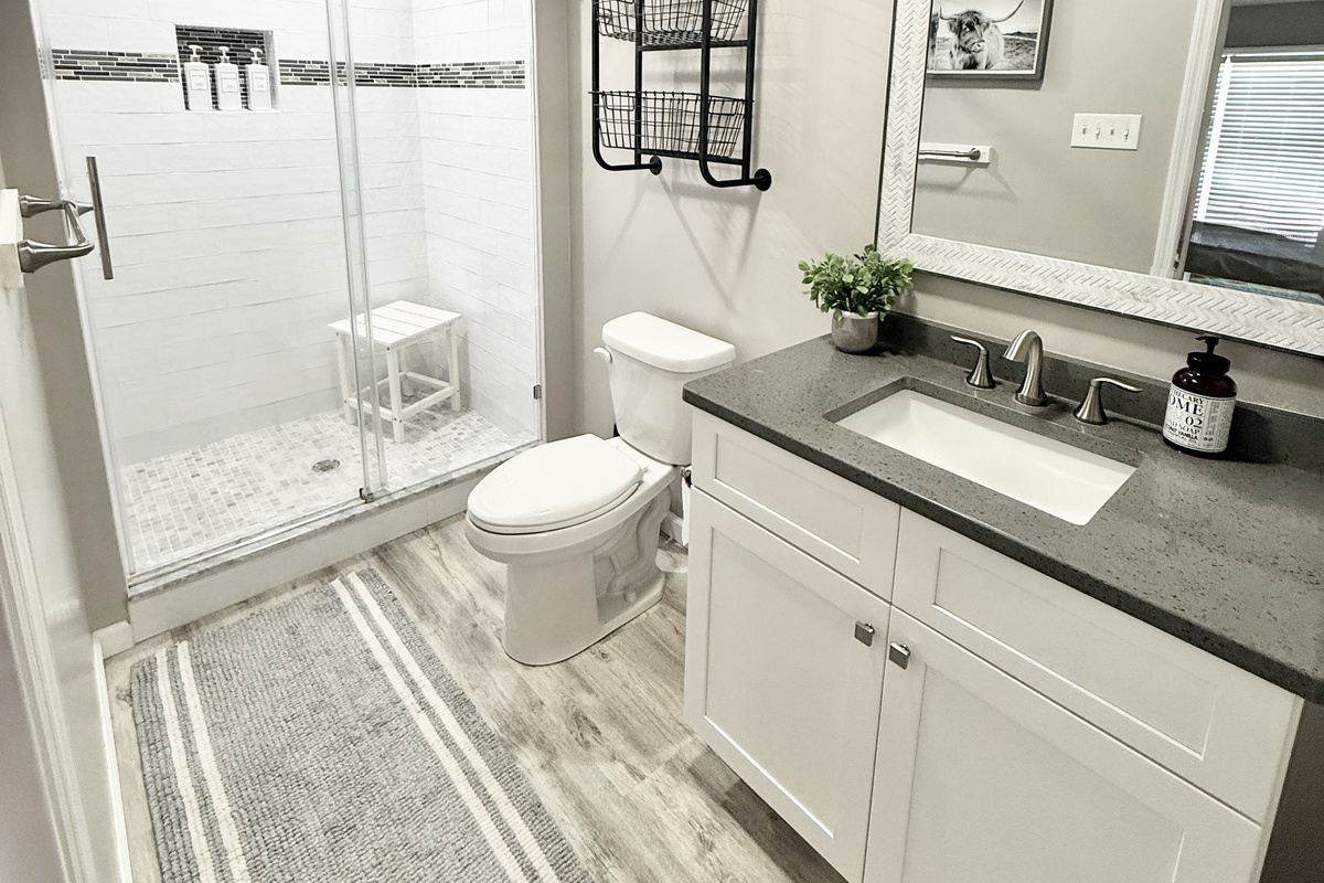 Refresh in our clean, updated bathroom featuring a spacious walk-in glass shower with sleek white subway tile and a decorative mosaic border. The shower is equipped with a convenient seat and plush charcoal towels for your comfort.