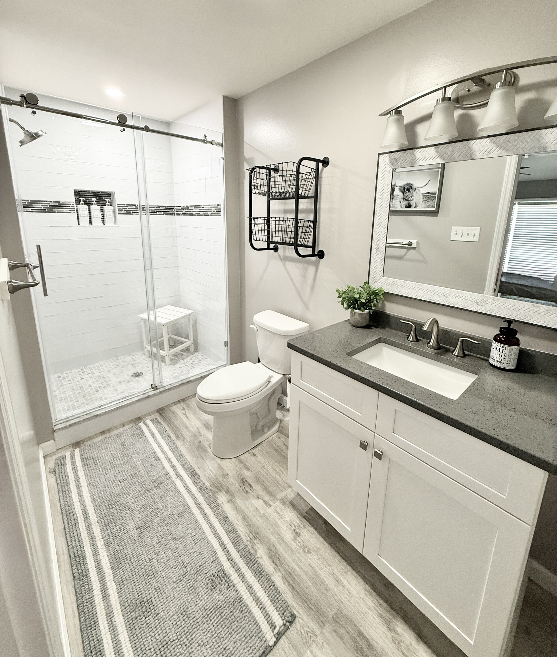 Refresh in our clean, updated bathroom featuring a spacious walk-in glass shower with sleek white subway tile and a decorative mosaic border. The shower is equipped with a convenient seat and plush charcoal towels for your comfort.