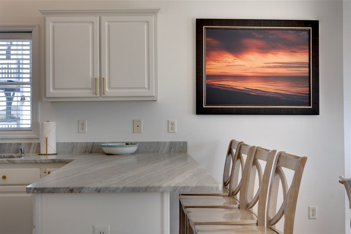 Bar seating for 4, and coastal art create a stylish spot for quick bites, cocktails, or sunset inspired dinners