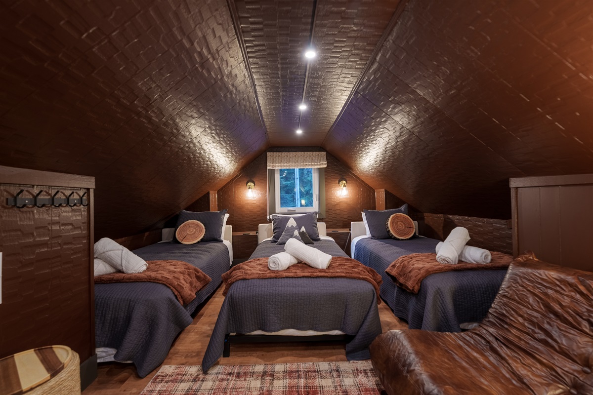 This charming attic hideaway features three twin beds under a sloped ceiling, creating a snug, sleepover-style space everyone loves.