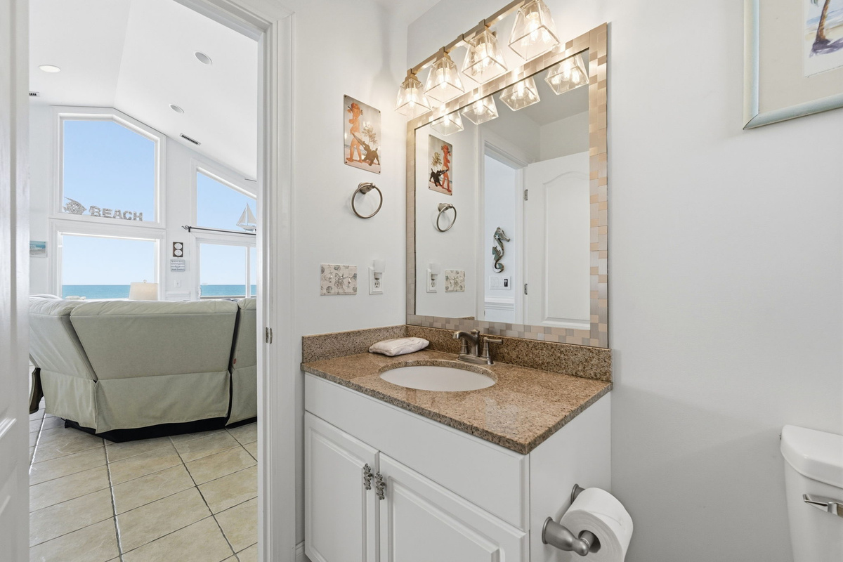 Bright bathroom vanity space with large mirror, granite countertop, and open view toward the main living area.