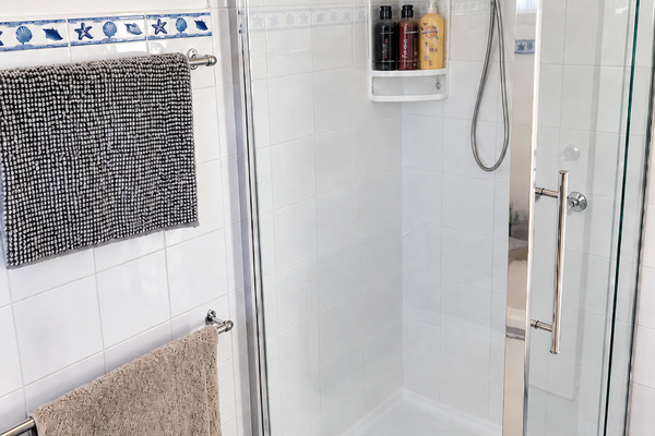 A bright and practical shower at Carlenes Getaway, featuring a glass enclosure, handheld showerhead and handy shelving for toiletries.