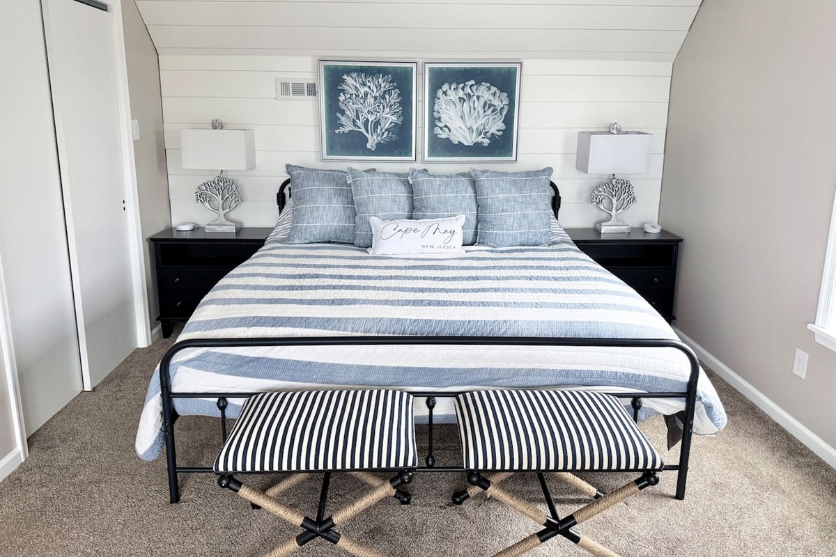 Discover a serene bedroom retreat designed with a calm, coastal aesthetic. The space features a cozy bed adorned with blue and white accents, framed by a charming shiplap wall, making it an ideal, restful sanctuary for your vacation.