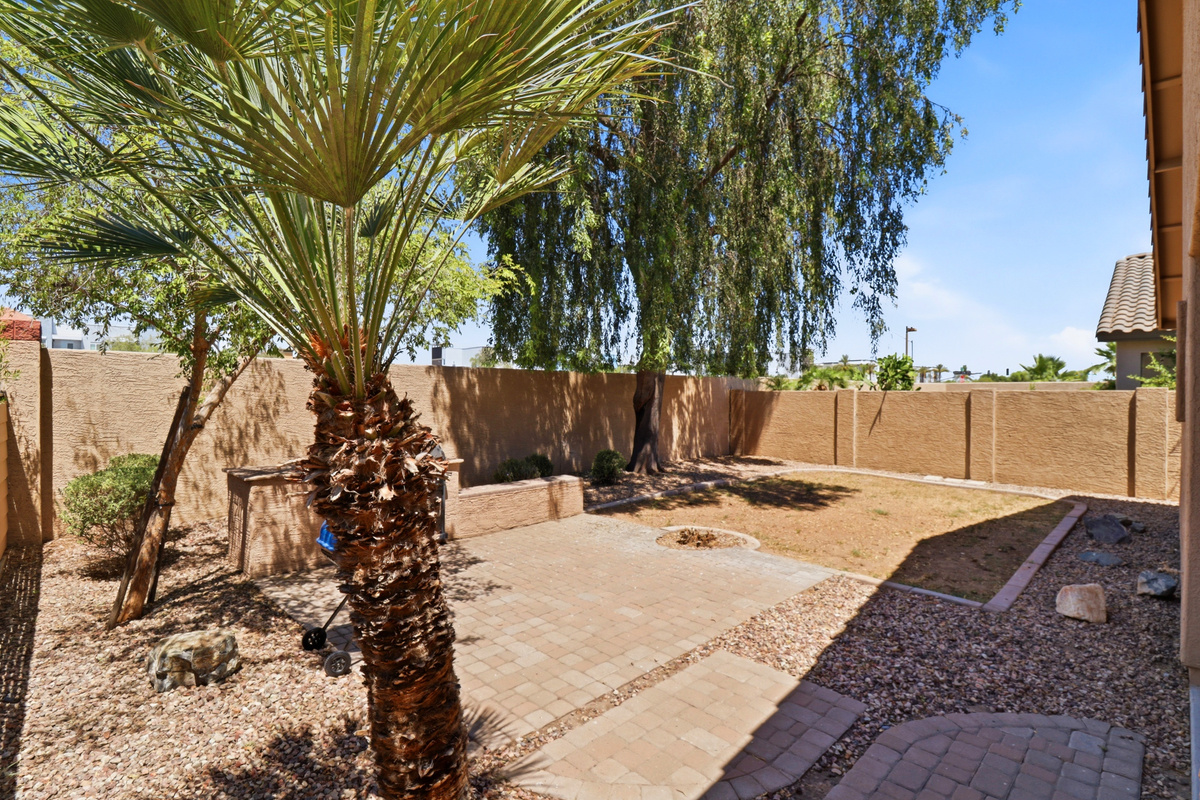 Fenced backyard with shade from the tree, a BBQ grill, and space to spend time outside.
