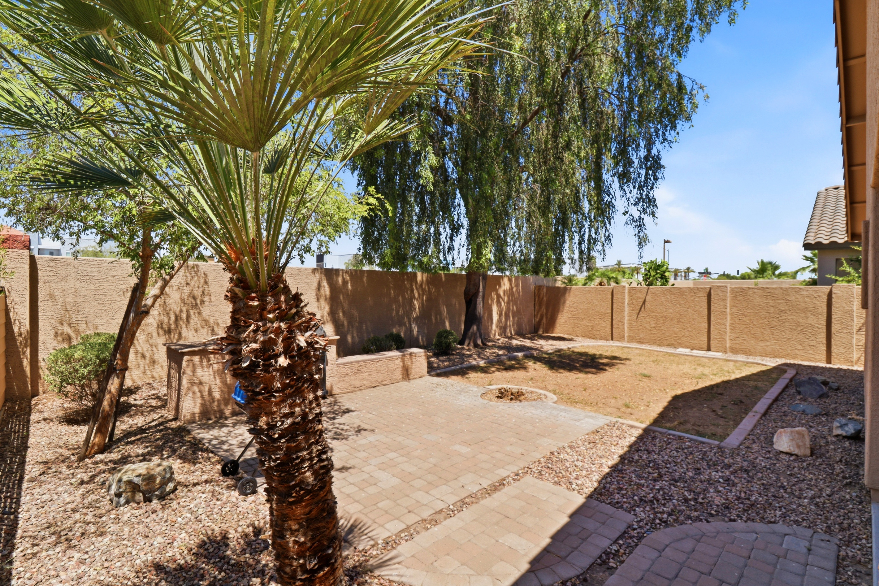 Fenced backyard with shade from the tree, a BBQ grill, and space to spend time outside.

