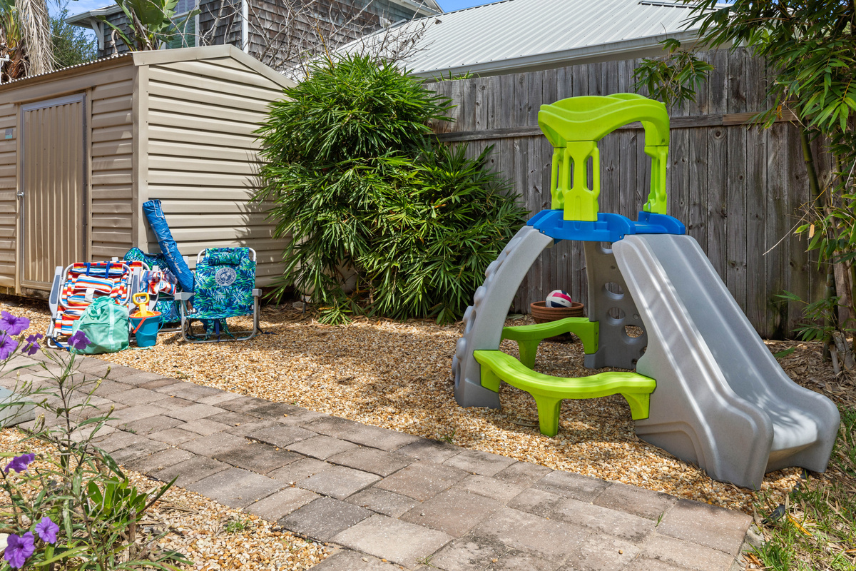 Beach chairs, an umbrella and sand toys sit by the shed, ready to grab on the way to the sand, next to a toddler slide.