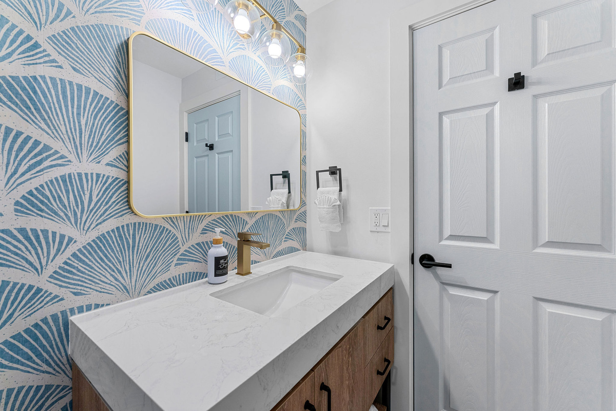 The master bathroom features tropical wallpaper, new tile and rich fixtures for a calming morning routine. Get ready for your evening out with plenty of counter space and bright lighting. A dedicated dark towel is provided for easy makeup removal.