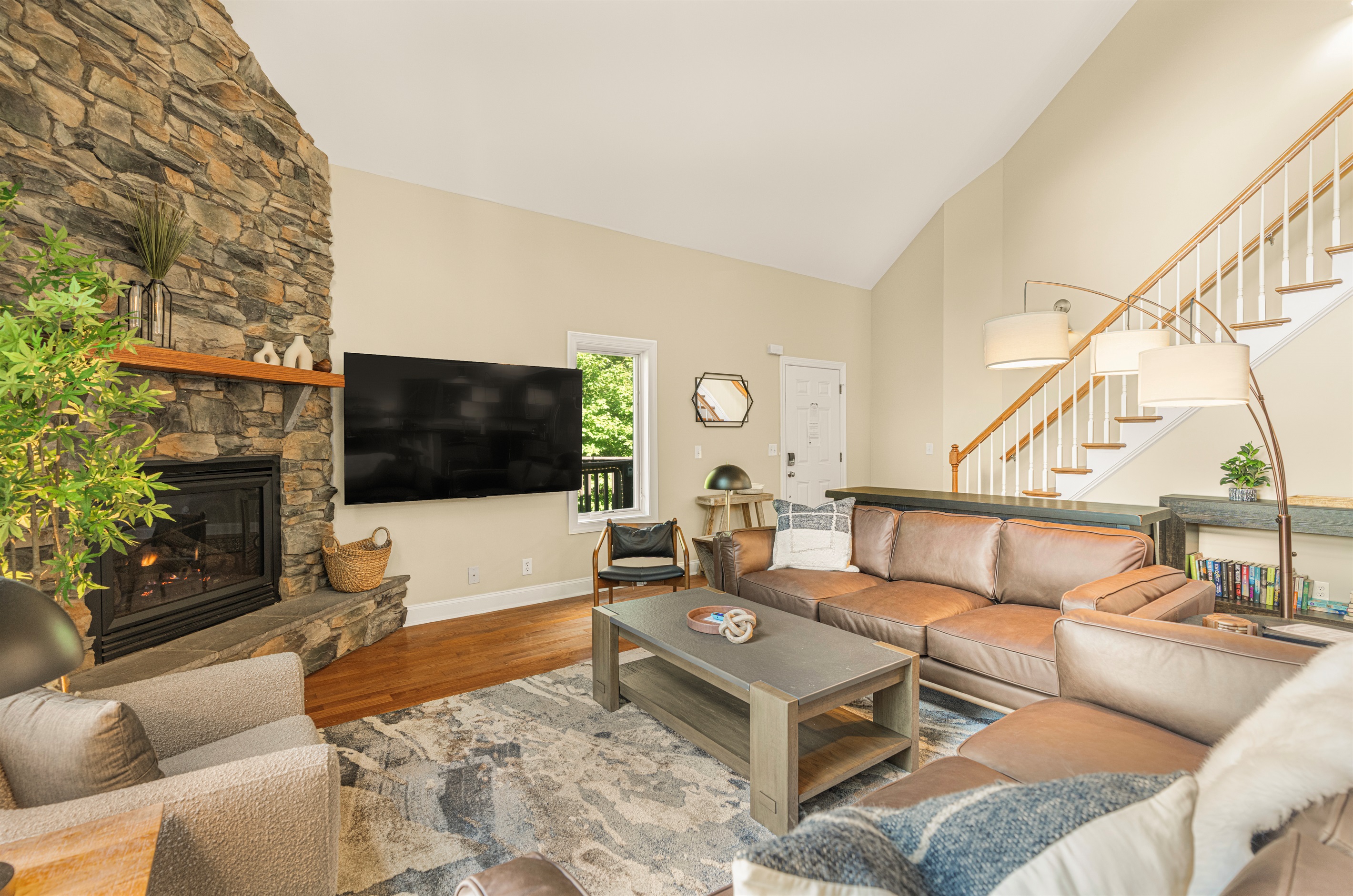 Spacious vaulted living room with two oversized leather sofas, smart TV, stone gas fireplace, and natural light—perfect for cozy evenings or streaming your favorite shows in comfort