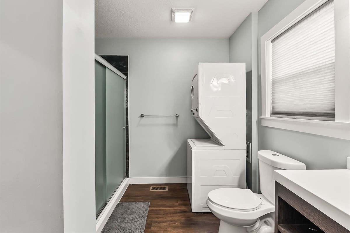 Full bathroom view showcasing the glass-enclosed shower, in-unit washer and dryer, and modern finishes.