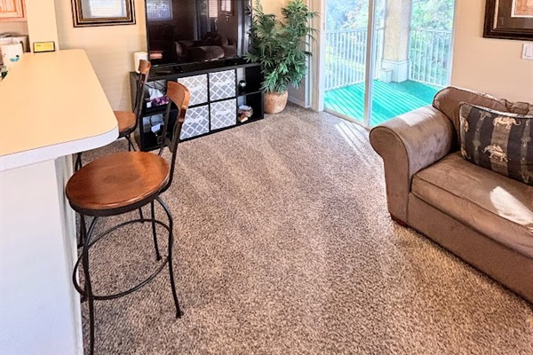Cozy living area with breakfast bar seating, large TV, comfortable sofa, and sliding glass doors leading out to the private balcony.