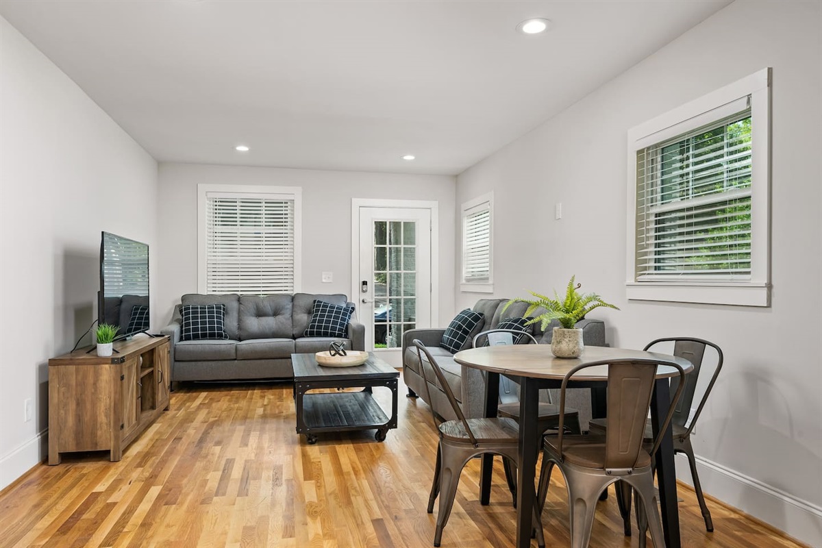 Spacious and bright, the combined living and dining space features contemporary furnishings, large windows that flood the room with natural light, and a dining table set for four.