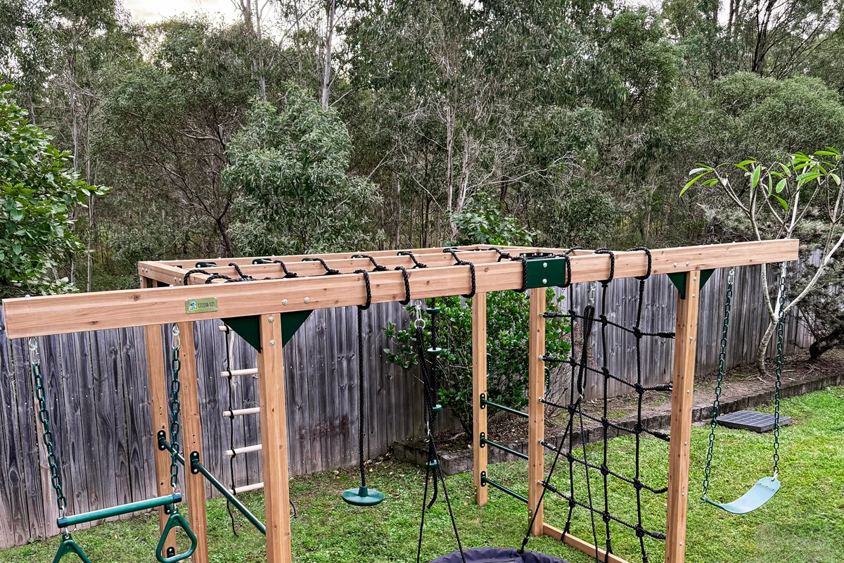 The jungle gym sits inside the fenced backyard, with swings, climbing sections and lawn space around the play structure.