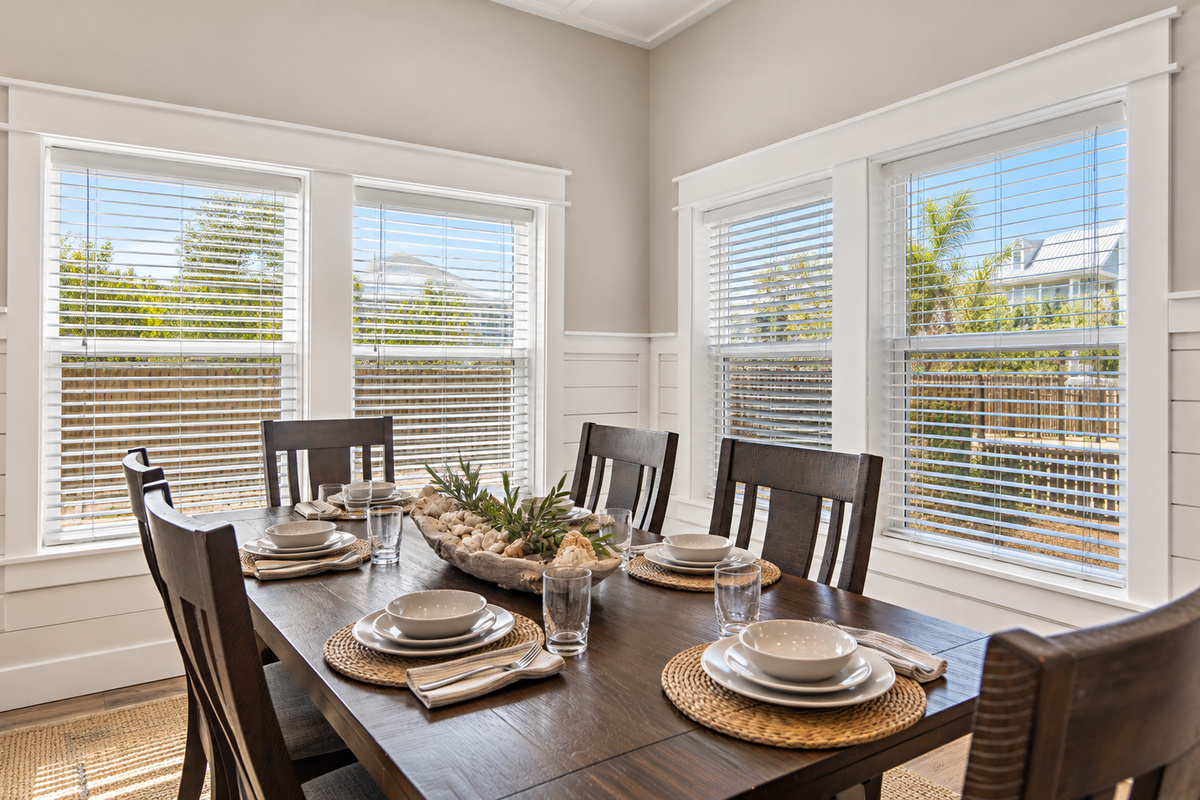 Bright, inviting dining area with a spacious table set for six, surrounded by natural light, coastal inspired details, and a comfortable open concept living space.