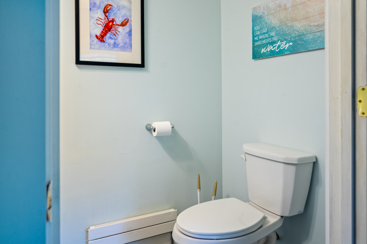 A close-up view details the clean toilet area within the first-floor half-bathroom. Equipped with an individual baseboard heating unit for seasonal comfort, this powder room space is finished with coordinated Maine coastal wall decor.