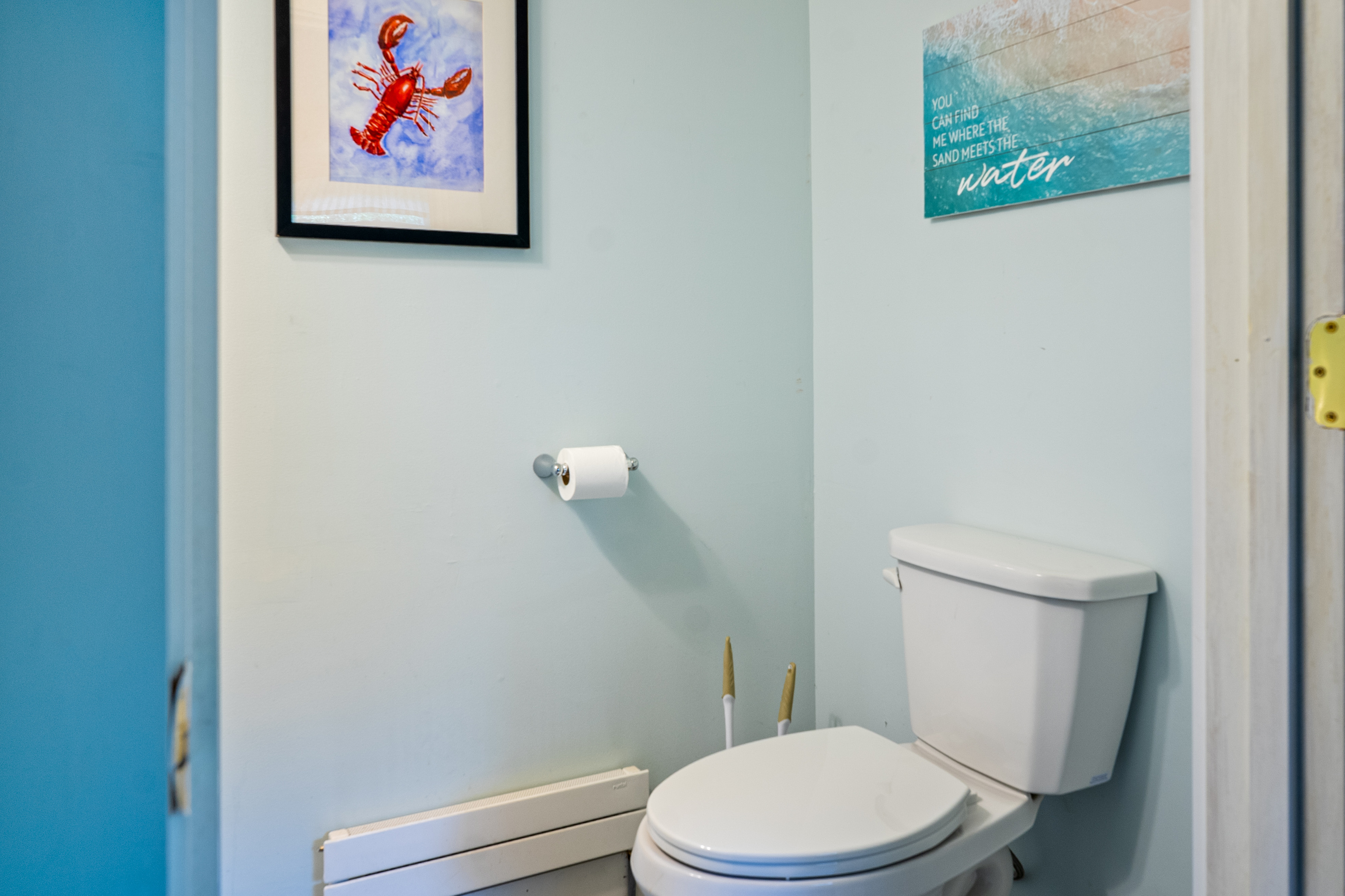 A close-up view details the clean toilet area within the first-floor half-bathroom. Equipped with an individual baseboard heating unit for seasonal comfort, this powder room space is finished with coordinated Maine coastal wall decor.