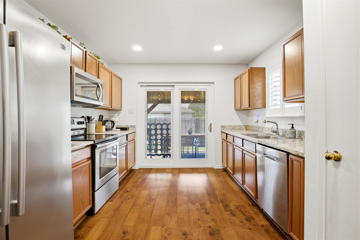 Stainless kitchen with electric stove, full-size refrigerator, microwave, and granite countertops — open to the dining and living area for easy entertaining. Fully stocked with cooking basics and utensils.