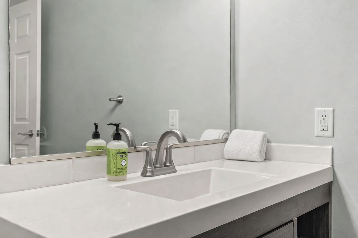 Close-up of the sink and vanity featuring a modern faucet, clean countertop, and provided hand soap.