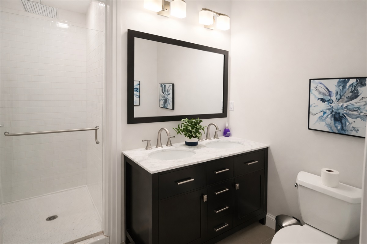 Refresh in the spacious main bathroom, featuring a double vanity with marble tops and a large glass-enclosed walk-in shower.