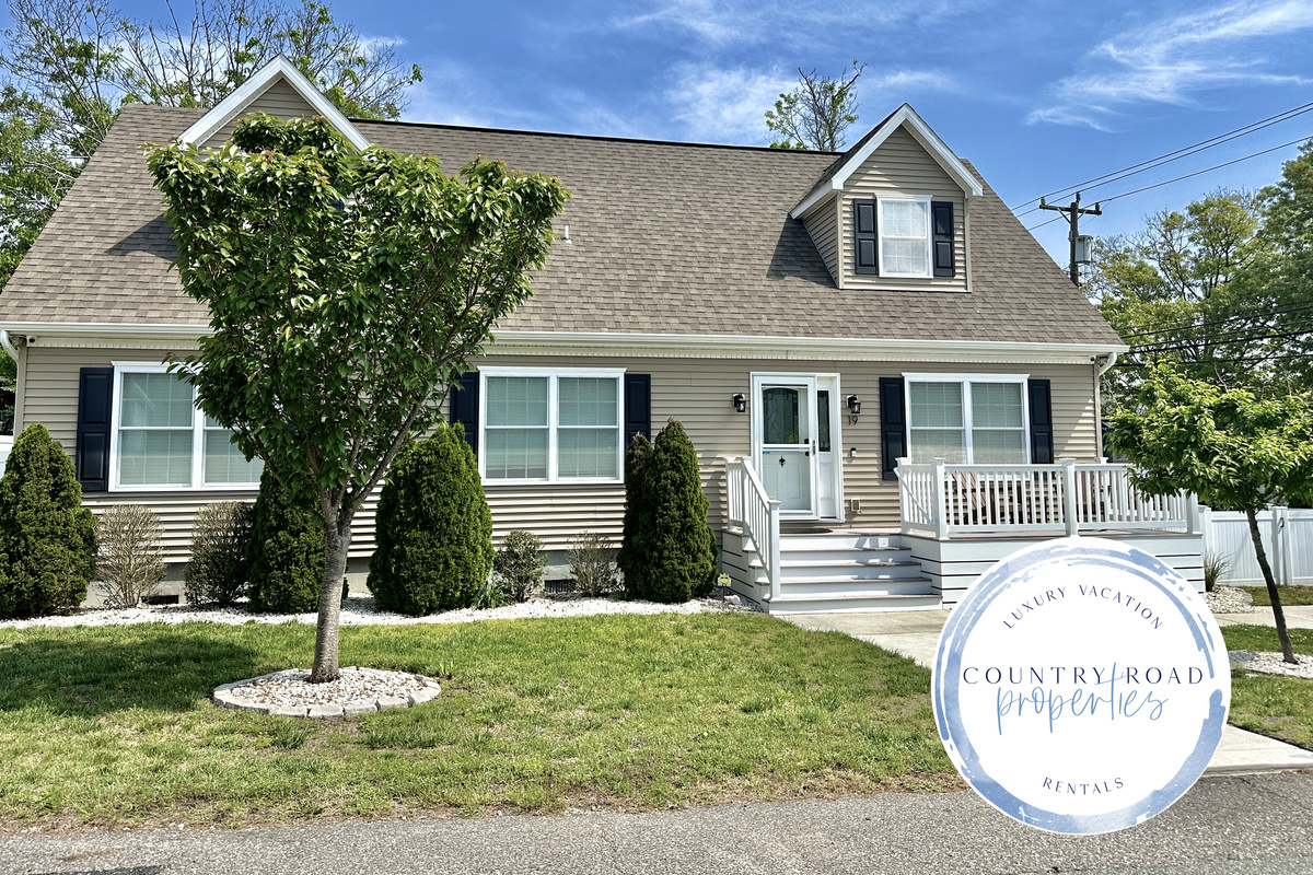 This welcoming home features a clean tan exterior with a small front porch and white railings. The property includes a green lawn, several evergreen shrubs, and a concrete walkway leading to the front door.