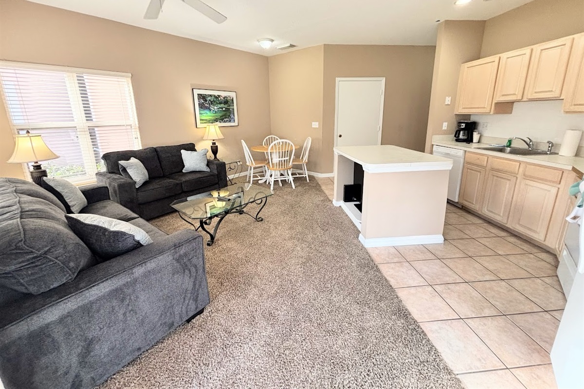 Open-concept living, dining, and kitchen area with comfortable seating, tile and carpet flooring, and a bright, functional layout.