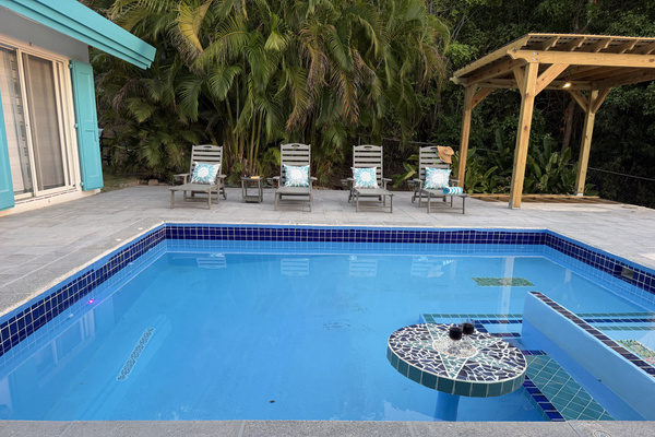 A tiled, circular swim-up table set inside the water, perfect for resting drinks or enjoying evening cocktails. A wooden gazebo with overhead lighting, offering shelter and cozy evening illumination beside the deck