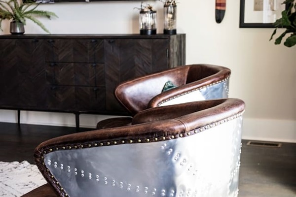 - Sleek leather armchairs with metal rivet accents add vintage aviation inspired character - Polished metallic backrests & rich brown leather bring texture & style to the space - Positioned perfectly for conversation or TV viewing in the living area