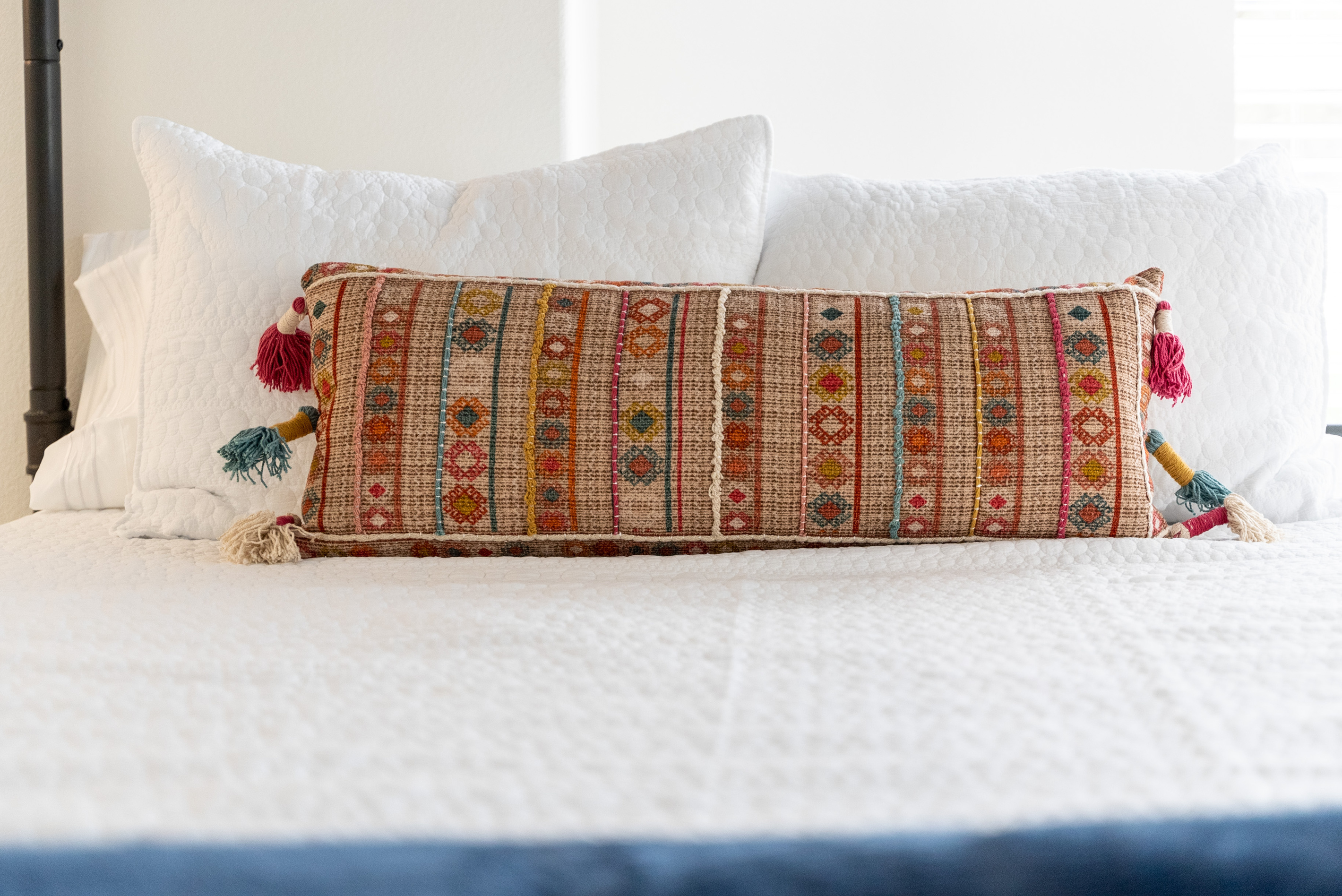 A colorful embroidered bolster pillow adds global charm to the bedding
